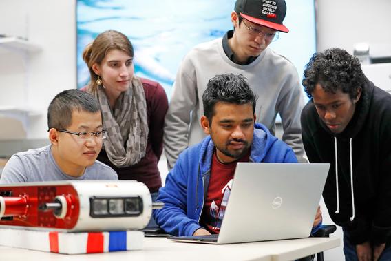 Five students working together around a laptop computer